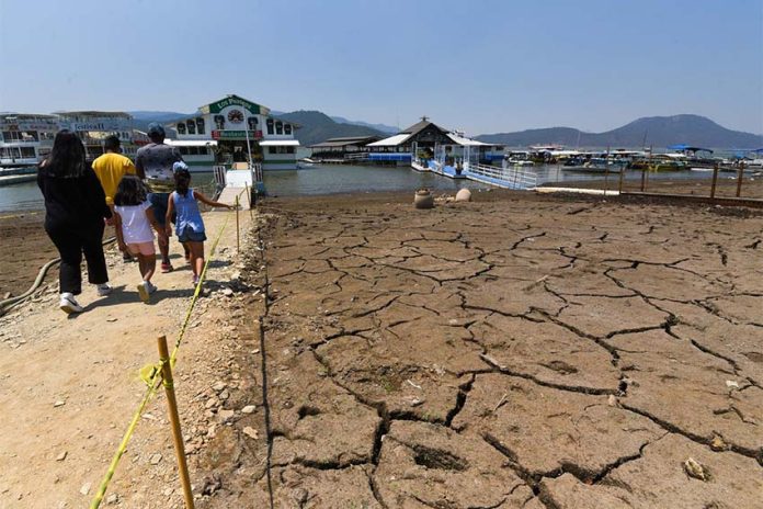 Family walking toward a marina in the Miguel Aleman reservoir in Mexico state. The lake bed they are walking on is cracked mud with no water.